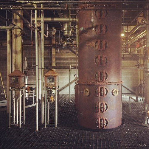 A complete Tier-3 setup — 10-15 gallon kettle with vertical packed column 4-6 feet tall, dephlegmator at the top with visible water connections, main condenser and parrot below it, PID controller on the side